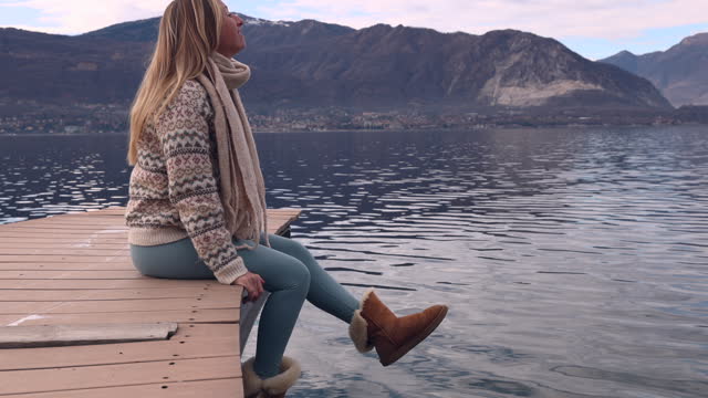Woman sitting on wooden platform above lake contemplates the scenery