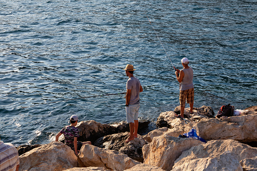 ANTALYA, TURKEY - JULY 08, 2018: Unknown fishermen with fishing rods are fishing in the Mediterranean Sea near Antalya.