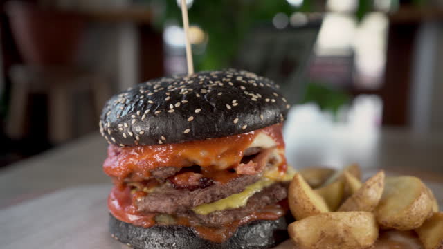 Tasty craft burger with black bun and fries served on wooden table in fast food restaurant