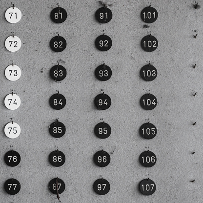 Black and white shot of series of round number tags arranged in rows and columns on a wall.