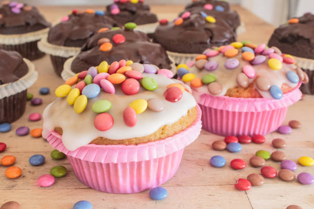 Various muffins lie decorated on a wooden table in a small bakery