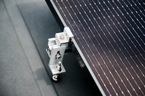 Close up of solar panel, securely fastened with robust mounting clamp to supporting structure on rooftop of house. Bolts and clamps provide stability and durability to solar installation.