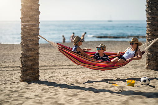 Three kids resting on beach hammock. Sunny summer vacations day at beach and sea.\nShot with Nikon D810