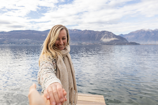 Follow me to concept, POV couple holding hands on wooden dock above lake