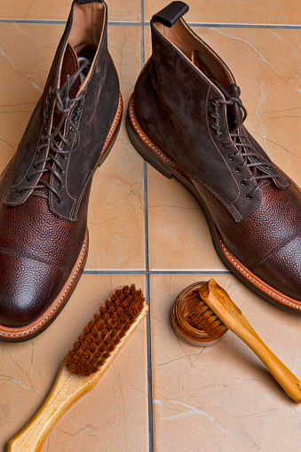Various Shoes Cleaning Accessories for Dark Brown Grain Brogue Derby Boots Made of Calf Leather Over Tile Background with Special Tools. Vertical Image Composition
