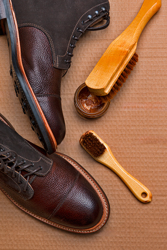 View of Various Shoes Cleaning Accessories for Dark Brown Grain Brogue Derby Boots Made of Calf Leather Over Paper Background with Cleaning Tools. Vertical Image