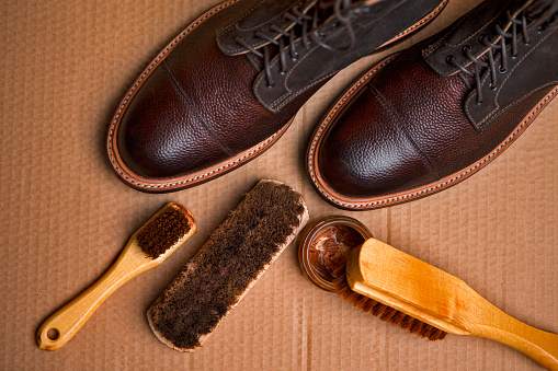Various Shoes Cleaning Accessories for Dark Brown Grain Brogue Derby Boots Made of Calf Leather Over Paper Background with Cleaning Tools. Horizontal Shot