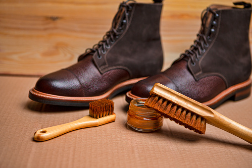 View of Various Shoes Cleaning Accessories for Dark Brown Grain Brogue Derby Boots Made of Calf Leather Over Paper Background with Cleaning Tools. Horizontal Composition