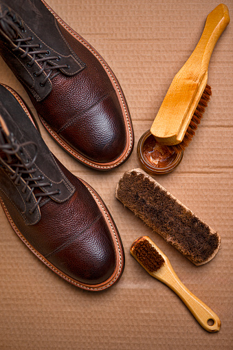 Upper View of Various Shoes Cleaning Accessories for Dark Brown Grain Brogue Derby Boots Made of Calf Leather Over Paper Background with Cleaning Tools. Vertical Shot