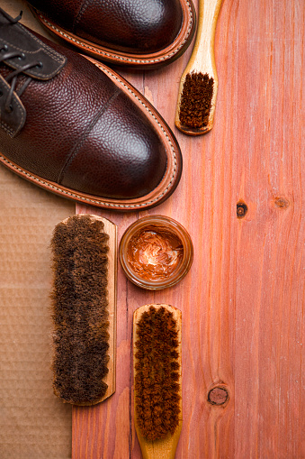 Flatlay of Various Shoes Cleaning Accessories for Dark Brown Grain Brogue Derby Boots Made of Calf Leather Over Paper Background with Cleaning Tools.Vertical Image