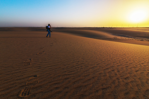 Photographer stands alone in the Desert leaving food steps in Dammam Saudi Arabia. Beautiful Sunrise background with sand dune structure