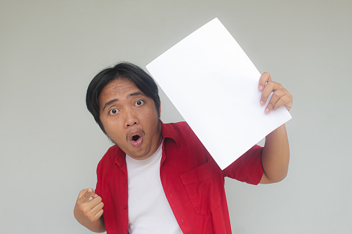 Close up portrait of young Asian man showing blank white paper with happy and wow expression.