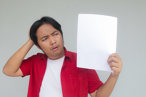 Close up portrait of young Asian man showing blank white paper with stressed expression.