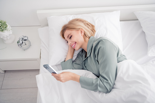 Photo portrait of blonde attractive young woman lying bed influencer dressed stylish gray pajama light modern bedroom minimalist design.