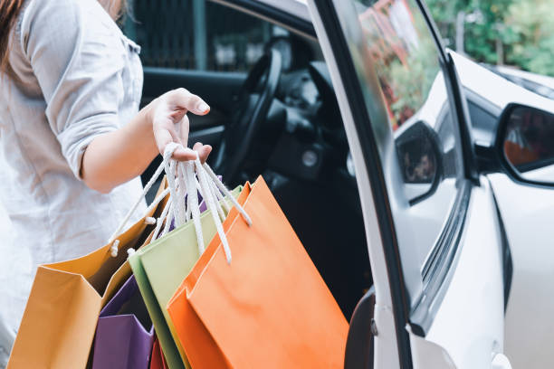 Close-up of a woman's hands placing colorful shopping bags into a white car after a shopping spree.