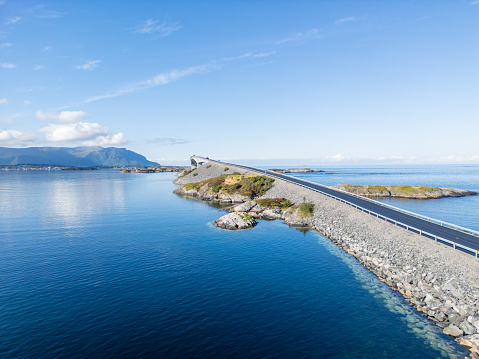 The bridge stretches over clear blue waters, linking rough little islands under a huge sky. Its modern design and smooth road look like a brush stroke on the natural scene. The bridge's soft curve and smart placement show how well it fits into the ocean setting.