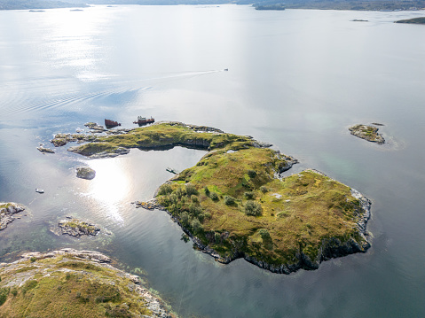 A lone house on a small island in the midst of a Norwegian fjord's still, reflective waters. The house is surrounded by  clear water and small grassy islands