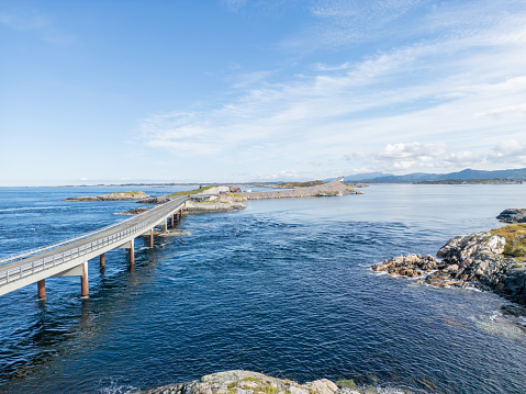 Close up side view of a bridge over clear blue sea waters, connected to a chain of rocky islands. The breathtaking natural seascape complements the bridge, all against a peaceful blue backdrop made by sky and sea.