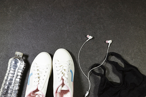 Healthy lifestyle, sport or athlete's equipment set : bottle of water with blue wireless headphone, sneakers on grunge gray background