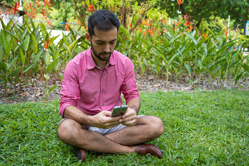 Man sitting on grass typing on smartphone