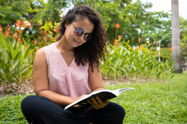 Woman reading book sitting on lawn in public park