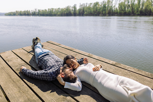 Mid adult interracial couple lying down on a pier by the lake. It's a beautiful sunny day, they look relaxed, happy and in love.