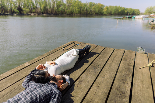 Mid adult interracial couple lying down on a pier by the lake. It's a beautiful sunny day, they look relaxed, happy and in love.