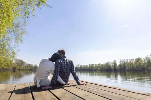 Mid adult interracial couple sitting on a pier by the river or lake. It's a beautiful sunny day, they look relaxed, happy and in love.