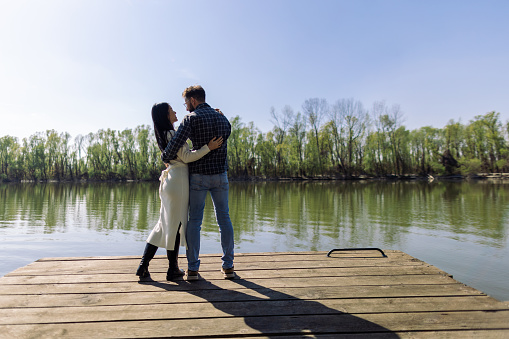 Mid adult interracial couple standing on a pier by the river or lake. It's a beautiful sunny day, they look relaxed, happy and in love.