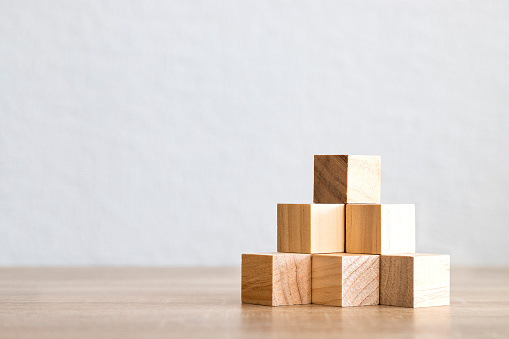 Wooden blocks arranged in a pyramid shape on a wooden surface with a plain background.