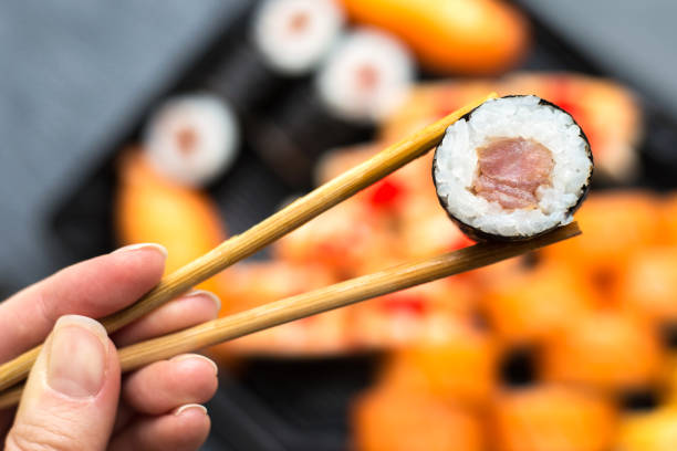 istock Women's hands hold sushi roll with sticks close up. Blurred dark background 2122767294