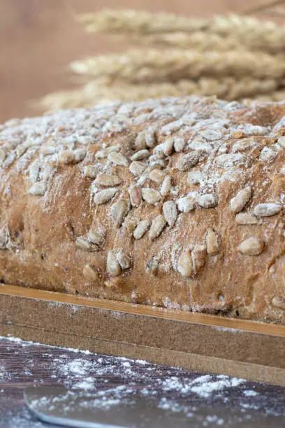Organic whole wheat loaf of bread with sunflower seeds and flour on wooden cutting board. Close-up. Selective focus. Eating healthy baked food.