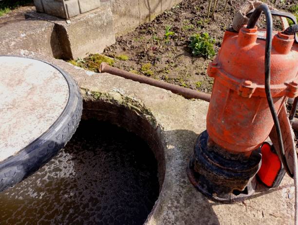 istock An orange water pump stands on a concrete base next to an open sewer pit for sewage pumping. Sewage service. 2122842551