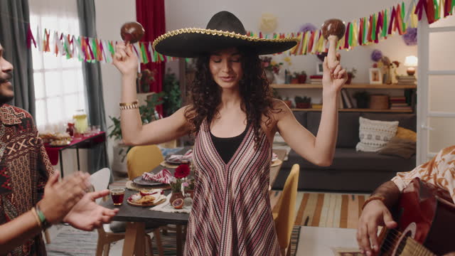 Portrait of Young Mexican Woman in Sombrero Dancing with Maracas at House Party
