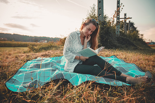Young woman reads a book on a picnic blanket on a meadow