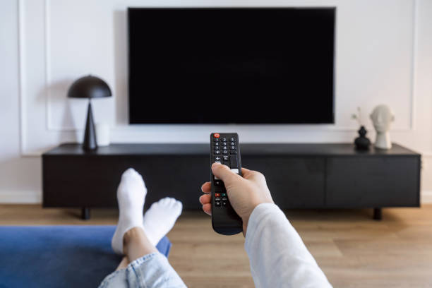 istock Woman hand hold remote control, turn on tv panel and relaxing on comfort sofa 2122898912