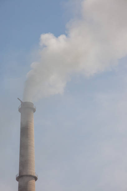 A tall chimney with smoke coming out of it. The sky is blue and the clouds are white