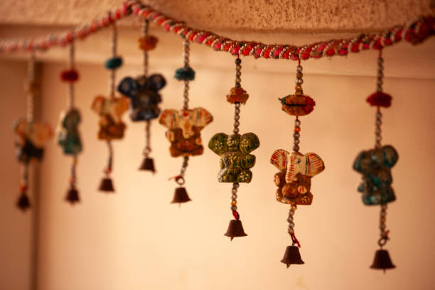 A row of bells hang from the ceiling, each with a different colored elephant head. The bells are hanging in a line, with some hanging higher than others. The elephants are all different sizes