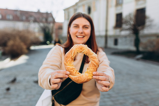 Attractive young female 30s tourist is holding precel, traditional polish snack in Krakow. Traveling Europe in spring. Selective focus. High quality photo