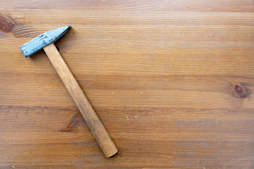 A blue-handled hammer lies on a wooden surface. The hammer is the focal point of the image, showcasing its sturdy construction and practical design.