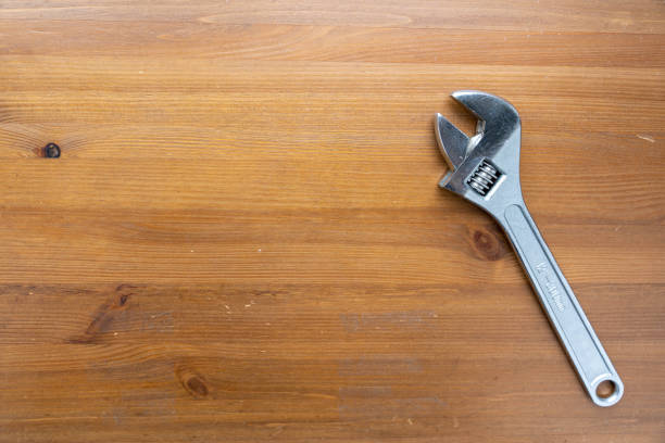 A wrench lays flat on top of a simple wooden table, casting a shadow in the light.