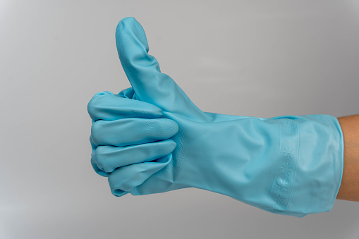 woman's hand wearing turquoise rubber gloves gesturing a thumbs-up sign against a clean, white background. The gloves are bright and the hand is well-manicured.