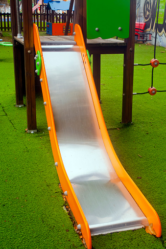 Metal yellow sledge, green soft flooring,  part of a children playground, outdoor play equipment, public park . Tui, Pontevedra province, Galicia, Spain.