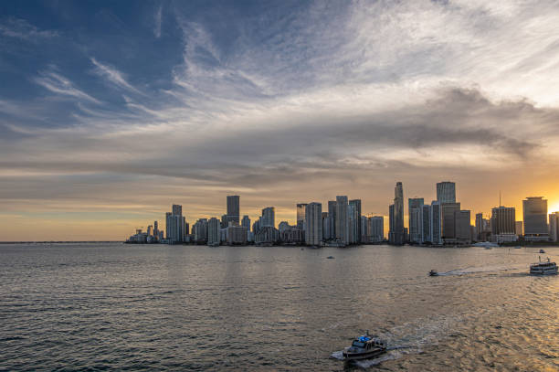 Miami, Florida, USA - July 29, 2023: Ground level sun behind Biscayne blvd 2/6, tall modern buildings form line behind Bayfront park and bay with yachts sailing. Entire coastline to south