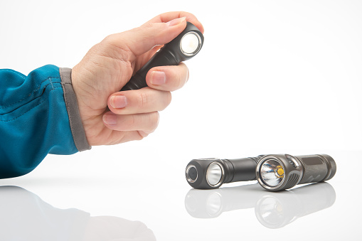 hand holds a flashlight against the background of other flashlights on a white background. camping and household item.