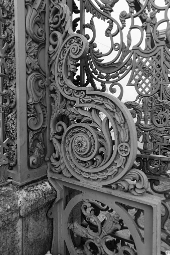 St. Petersburg, Russia, February 10, 2023. Fragment of a beautiful antique metal fence of a palace in the center of the city, complex floral ornament, cast iron, granite base, details and elements of architecture, fine workmanship, city decoration, vintage background, black and white stock photo.