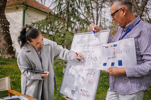 Small group of people on a outdoor meeting in nature using white board for making calculation