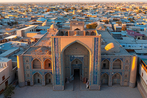 Ulugbek Madrasah in Bukhara in warm Sunset Light. Ulugbek Madrasah is an architectural monument from the year 1417. It is the oldest preserved madrasah in Central Asia. Giant decorated Iwan - Entrance into the historic islamic Medrassa - School Building in the Medina of Bukhara. Drone Point of View. Ulugbek Madrasah, Bukhara, Khorezm Region, Uzbekistan, Central Asia