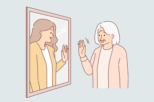 Elderly woman sees herself from past in reflection of mirror, and waves hand, receiving positive emotions from nostalgia. Granny with gray hair goes back to past enjoying memories of youth