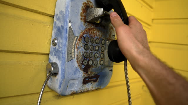 SLO MO Cropped Hand of Man Using Rusty Landline Phone Mounted on Yellow Wall in Booth